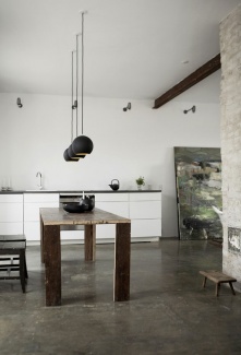 Ambiente súper rústico do estúdio Norm Architecture com mesa de madeira de demolição e piso em cimento queimado. Destaque para a obra de arte pintada pela proprietária