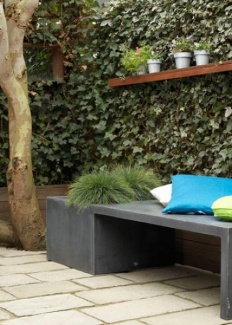 Muro verde com prateleira para as plantinhas e um banco de concreto com almofadas, simples e moderno! ótimo lugar para uma leitura.