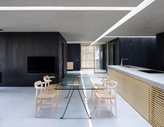 Cozinha com revestimento parede de madeira escura, em contraste com a leveza da mesa de vidro e balcão de concreto em ilha de cozinha.