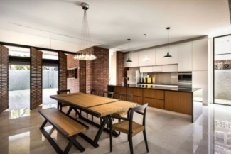 Cozinha com piso em cimento quemado e ilha com granito preto com montantes, armários brancos e paredes em tijolos aparentes.