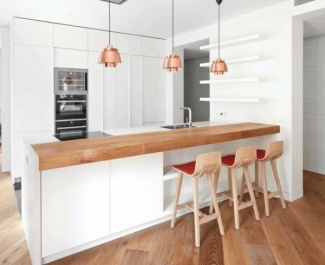 Piso e bancada de madeira, e armários e balcão da pia brancos, destaque para as luminárias pendentes em bronze.