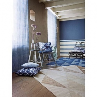 Sala praiana com cortinas e tapete azuis, almofadas estampadas para compor.