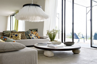 O centro de pés de pedra e a luminária de linha dão o charme nesta sala branca e iluminada.