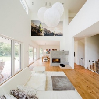 Sala branca com piso de madeira. Sofá e tapete brancos, e um discreto centro de concreto.